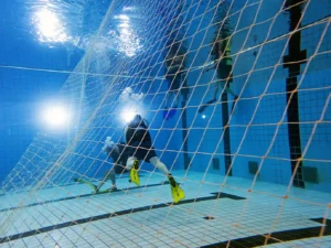 Amphibius Nettentraining - duikers zwemmen onder water in het zwembad achter een groot net