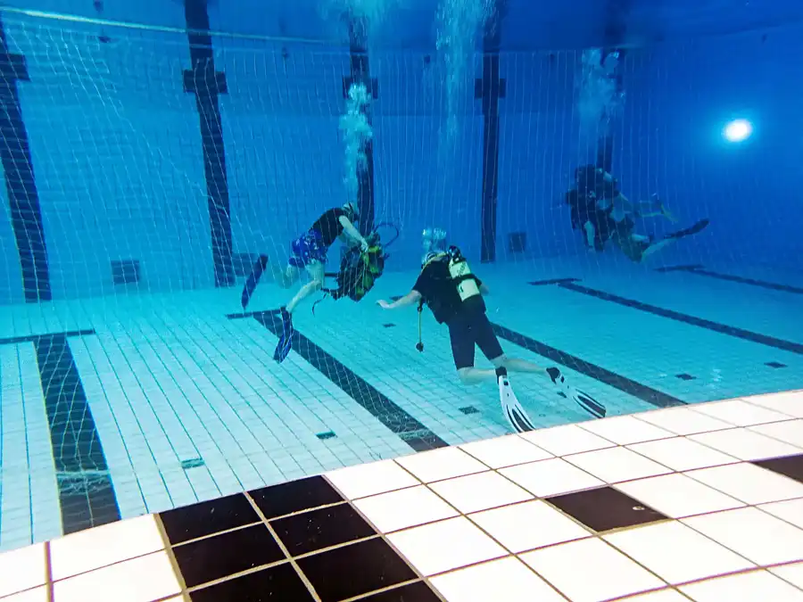 Nettentraining - een duiker maakt zwevend onder water zijn duikset los uit een net terwijl zijn duikbuddy toekijkt